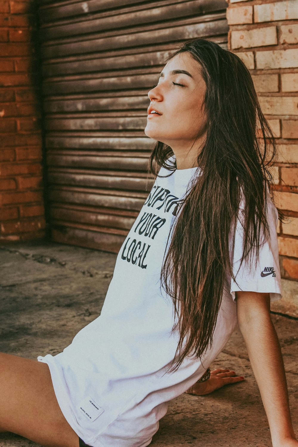 woman wearing white and black shirt sitting on gray concrete