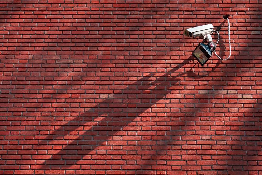 câmera CCTV cinza ao lado da parede de tijolos vermelhos