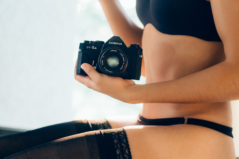 Donna che indossa reggiseno nero che tiene la macchina fotografica nera