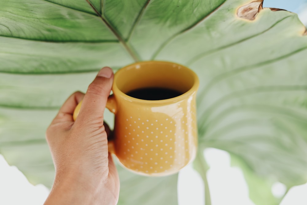 yellow ceramic mug on left human hand