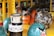 A collection of colorful ceramic objects arranged on yellow metal shelves. An orange creature with a wide grin sits among patterned vases and a round object decorated with abstract designs. A piece resembling a character with angry eyebrows features prominently in the foreground.