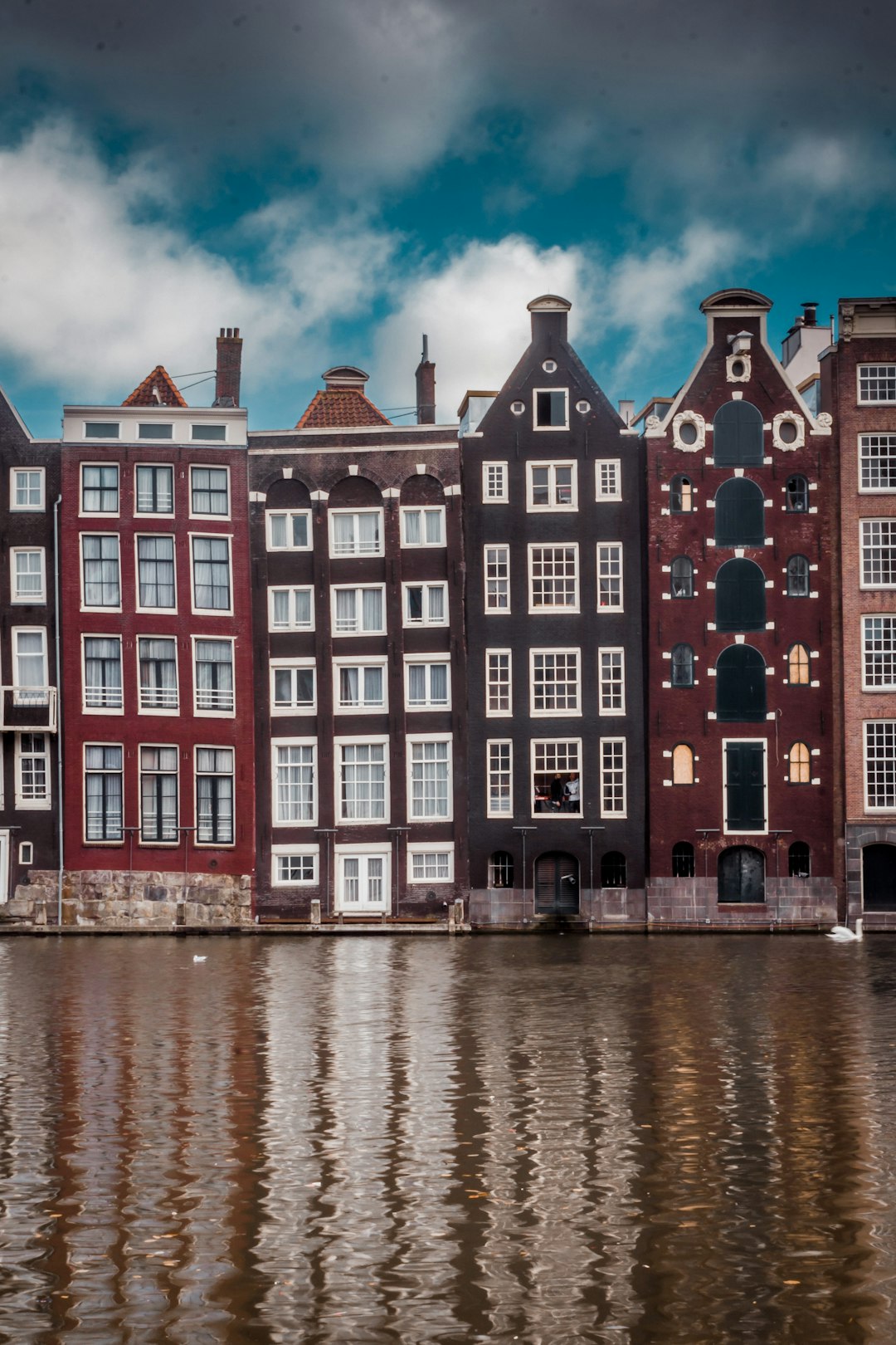 concrete buildings by the river under white clouds and blue sky during daytime