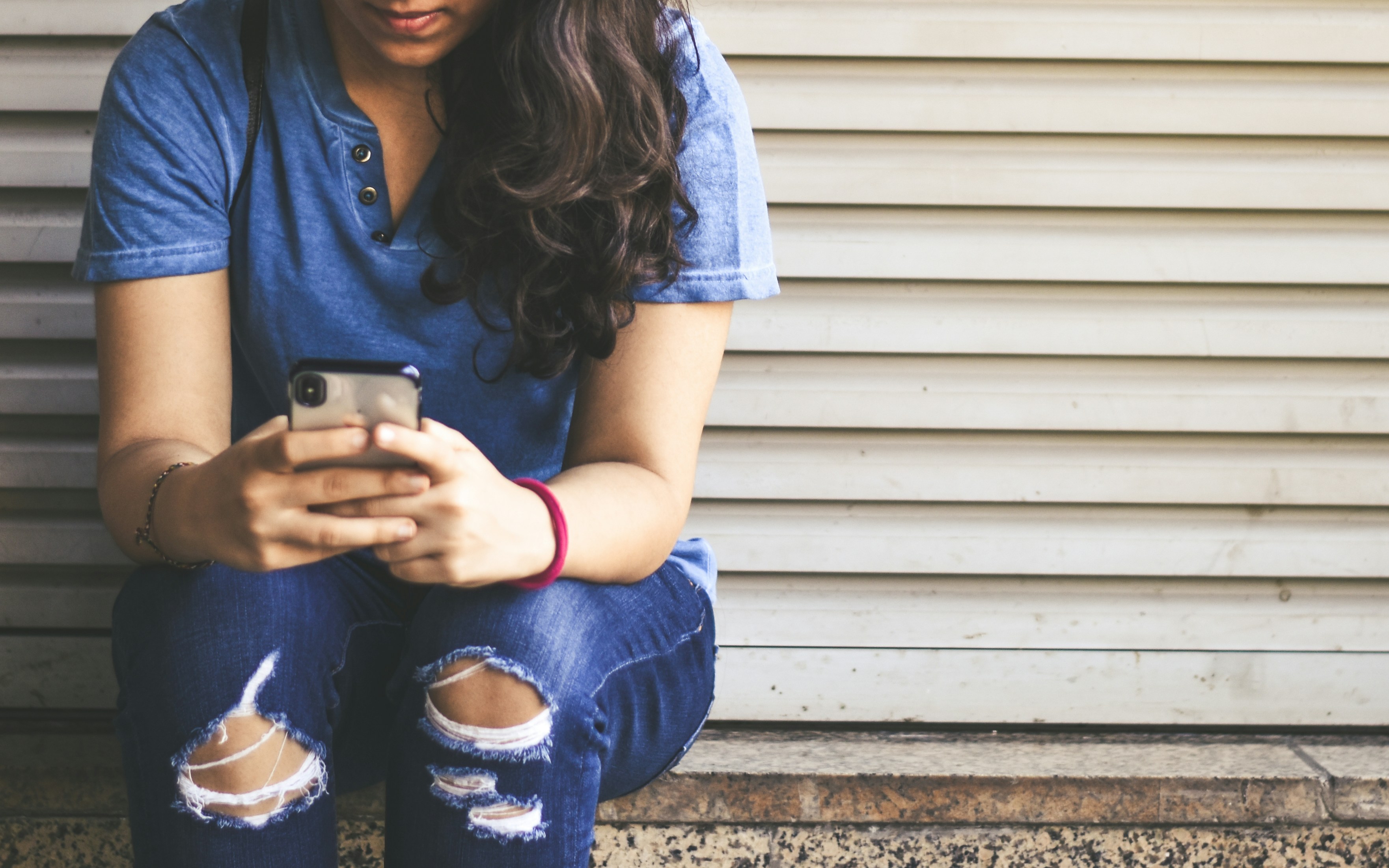 woman sitting beside white roller shutter while holding smartphone