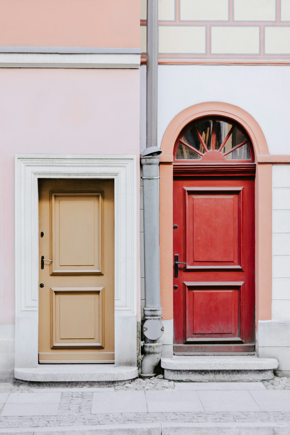 a red door and a yellow door in front of a pink building
