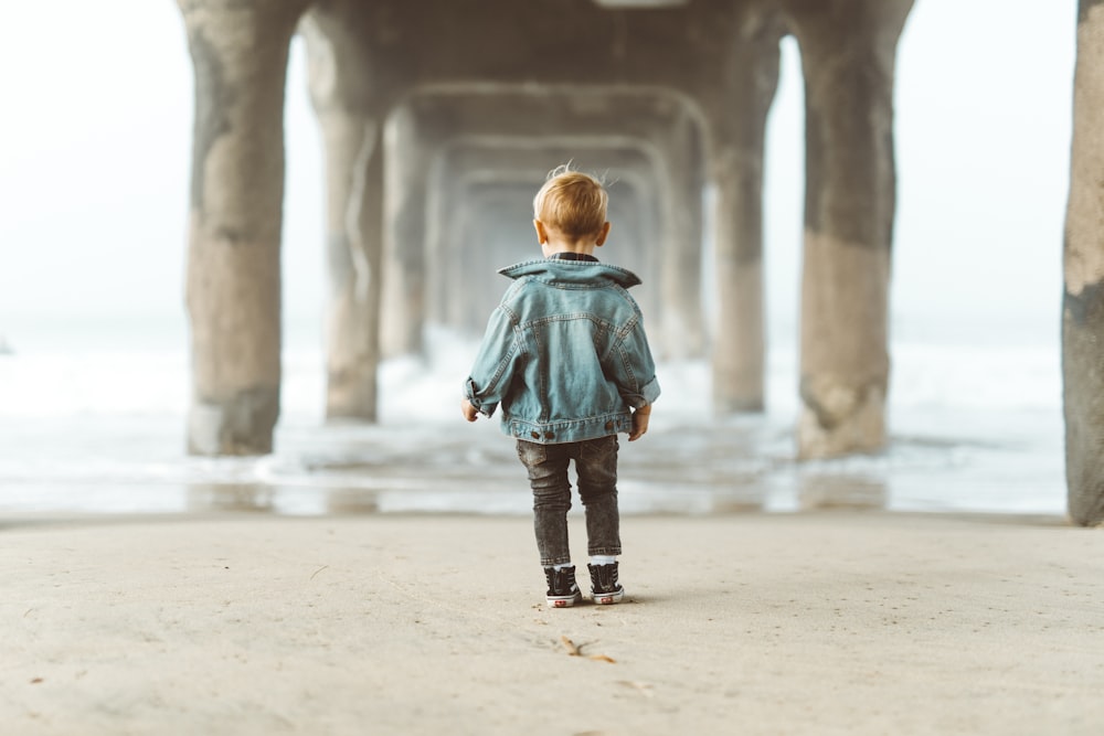 boy standing on seashore under dock during daytime