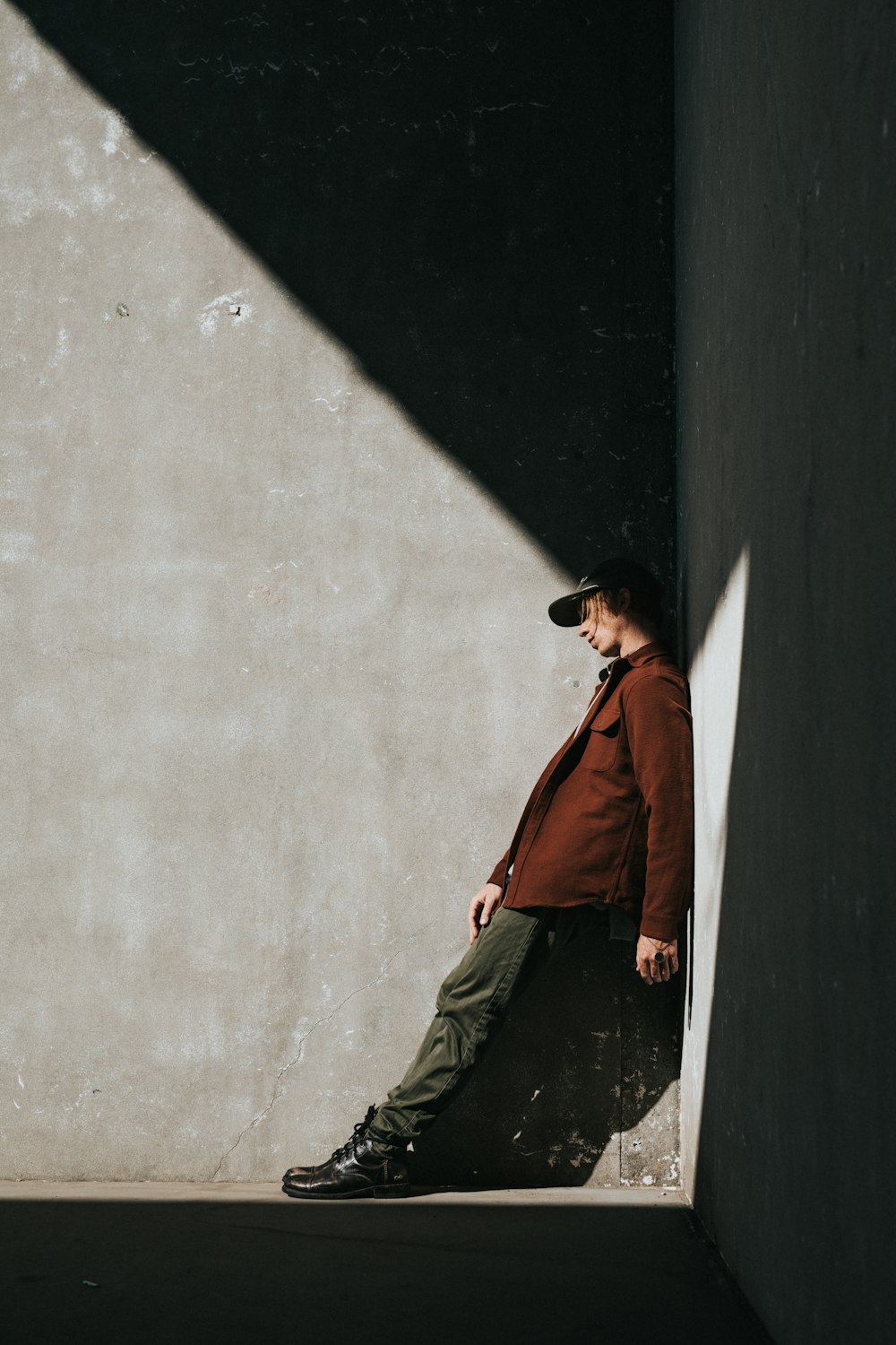 person wearing brown jacket leaning on gray wall