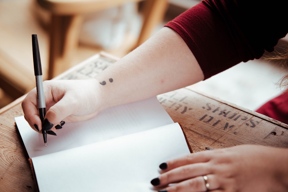 person holding pen above white open notebook page