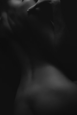 A black and white photograph showcasing a close-up view of a human form with soft lighting creating deep shadows and highlights, emphasizing the curves and contours of the body.