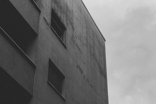 A black and white photograph capturing an empty urban corner with subtle shadows and textures.