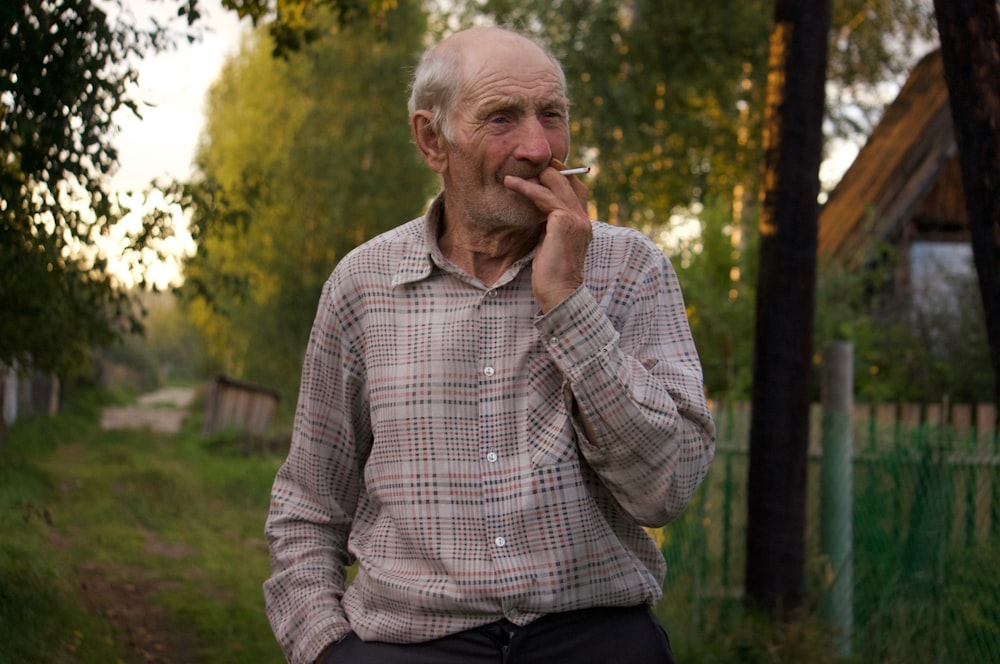 man in beige and red plaid long-sleeved collared shirt smoking cigarette during daytime