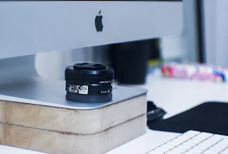 A candid shot of a camera resting beside a laptop on a minimalist wooden desk.