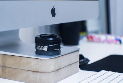 A candid shot of a camera resting beside a laptop on a minimalist wooden desk.