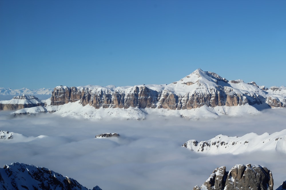 snow covered mountain above clouds under clear blue sky