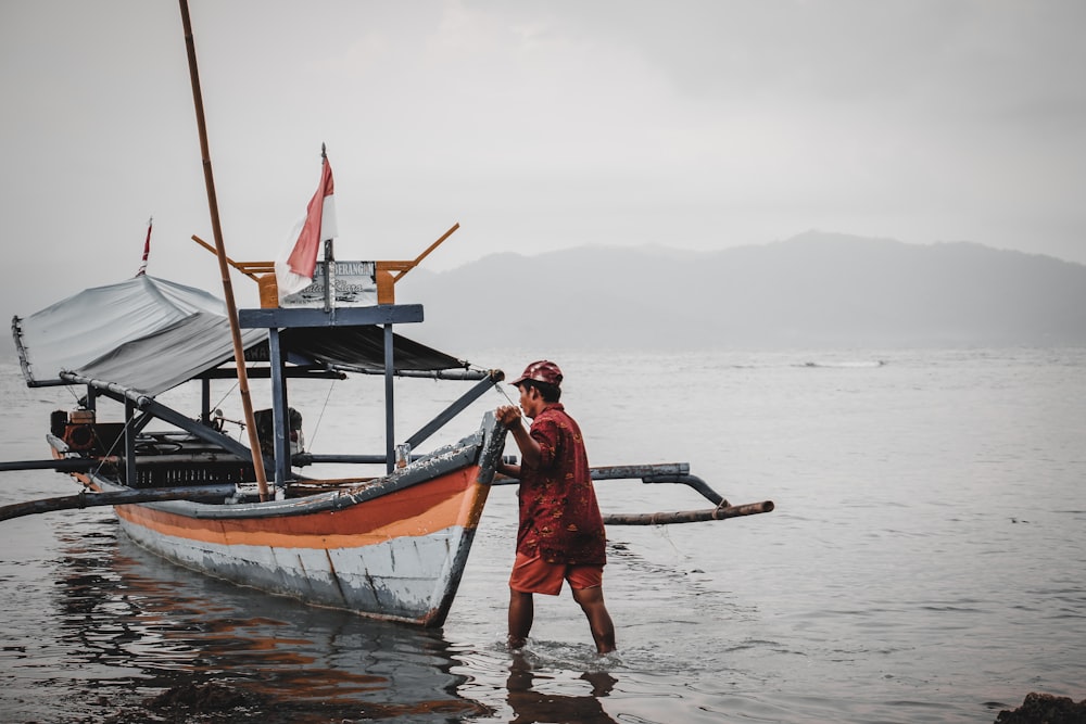 man standing beside boat at beach