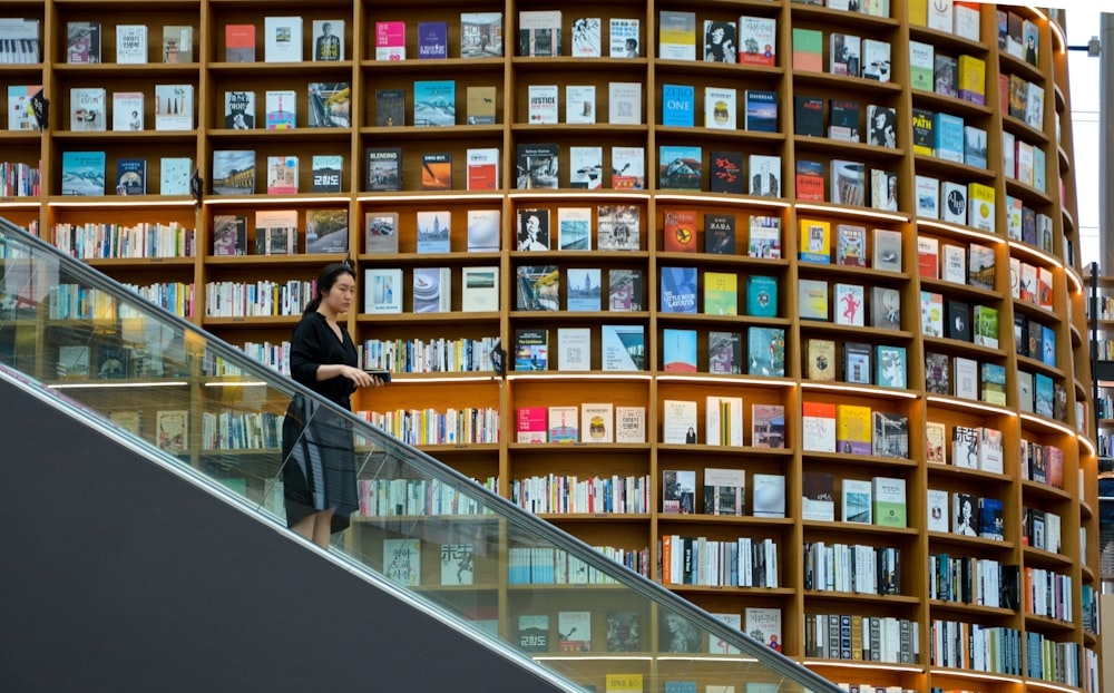 woman standing on escalator near brown wooden book shelves