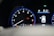 A car dashboard with a tachometer displaying RPM levels and warning lights illuminated, including oil and engine warnings. A digital screen shows the car in a parking mode with an open door and details like fuel range and comfort mode.