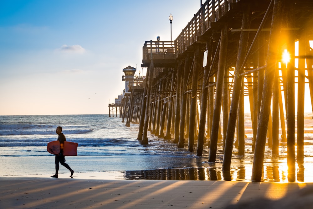 Hombre caminando en la playa mientras lleva bodyboard durante la hora dorada