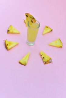 Bright yellow pineapple and lemon juice with tropical fruits on a light background.