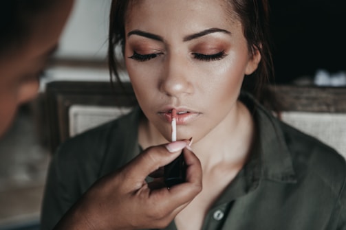 Behind-the-scenes photo of a makeup artist applying gloss on a model