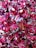 A collection of wrapped candies with shiny, metallic pink wrappers featuring decorative patterns and branding text. The candies are tightly packed together, creating a colorful and glossy surface.