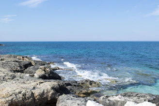 Crystal-clear ocean waves crashing against rugged cliffs under a bright blue sky