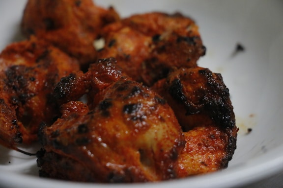 Juicy, grilled pieces of chicken with a deep reddish-brown hue, displaying charred edges and a savory appearance. The meat is served in a white bowl, highlighting its rich seasoning and crispy exterior.