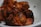 Juicy, grilled pieces of chicken with a deep reddish-brown hue, displaying charred edges and a savory appearance. The meat is served in a white bowl, highlighting its rich seasoning and crispy exterior.