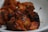 Juicy, grilled pieces of chicken with a deep reddish-brown hue, displaying charred edges and a savory appearance. The meat is served in a white bowl, highlighting its rich seasoning and crispy exterior.