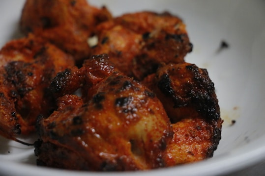 Juicy, grilled pieces of chicken with a deep reddish-brown hue, displaying charred edges and a savory appearance. The meat is served in a white bowl, highlighting its rich seasoning and crispy exterior.