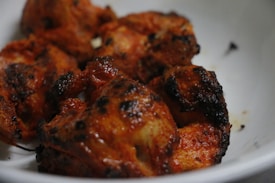 Juicy, grilled pieces of chicken with a deep reddish-brown hue, displaying charred edges and a savory appearance. The meat is served in a white bowl, highlighting its rich seasoning and crispy exterior.