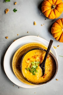 A warm bowl of homemade pumpkin soup with a swirl of cream and fresh herbs on a wooden table.