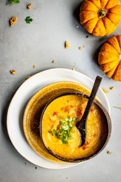 A steaming bowl of creamy pumpkin soup garnished with toasted seeds and fresh herbs.