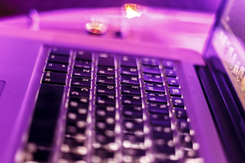 Close-up of hands typing on a laptop keyboard with black and purple tones