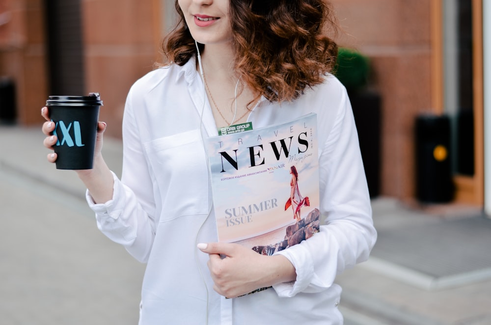 woman holding magazine and plastic tumbler