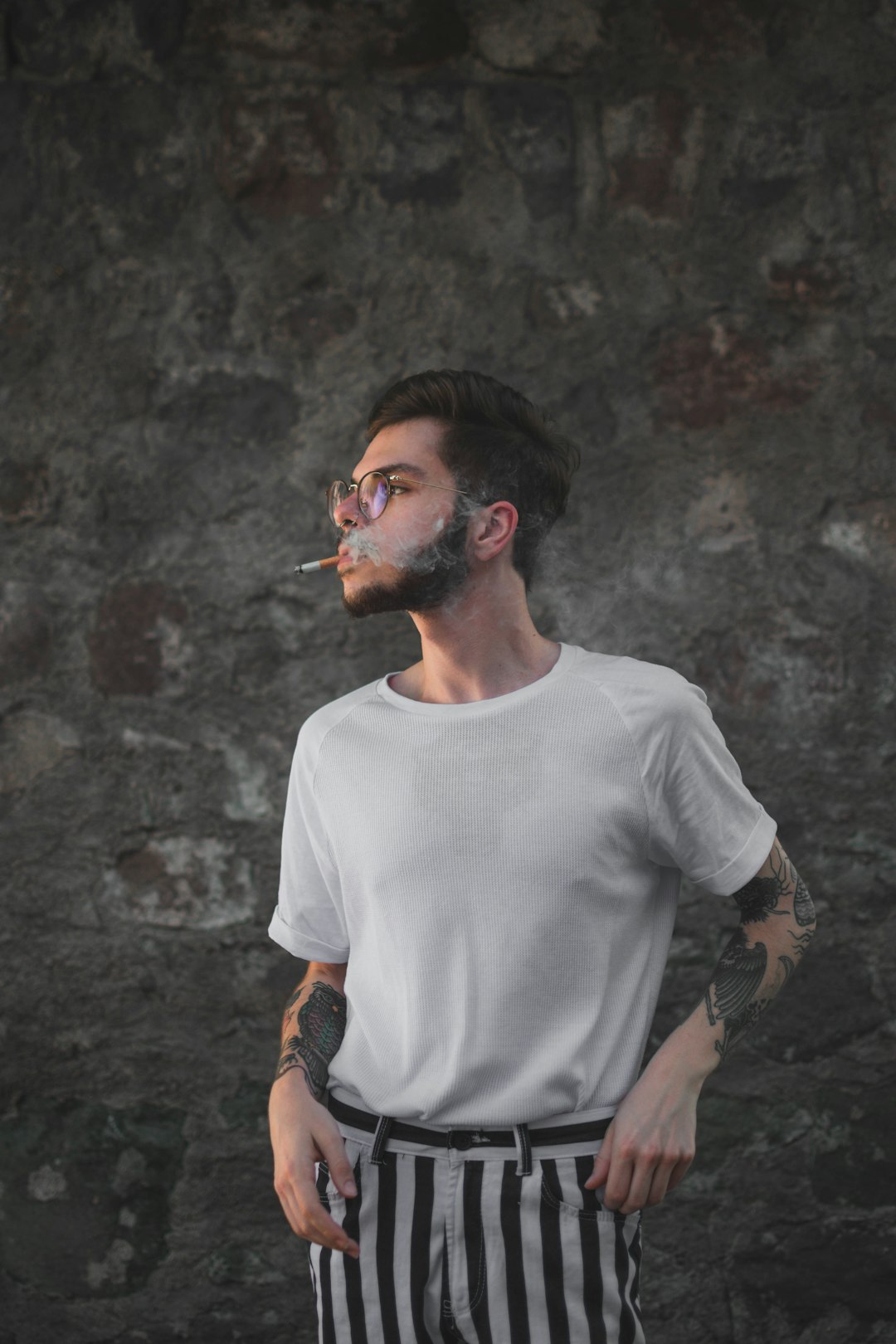 man in white crew-neck t-shirt and striped pants smoking by wall