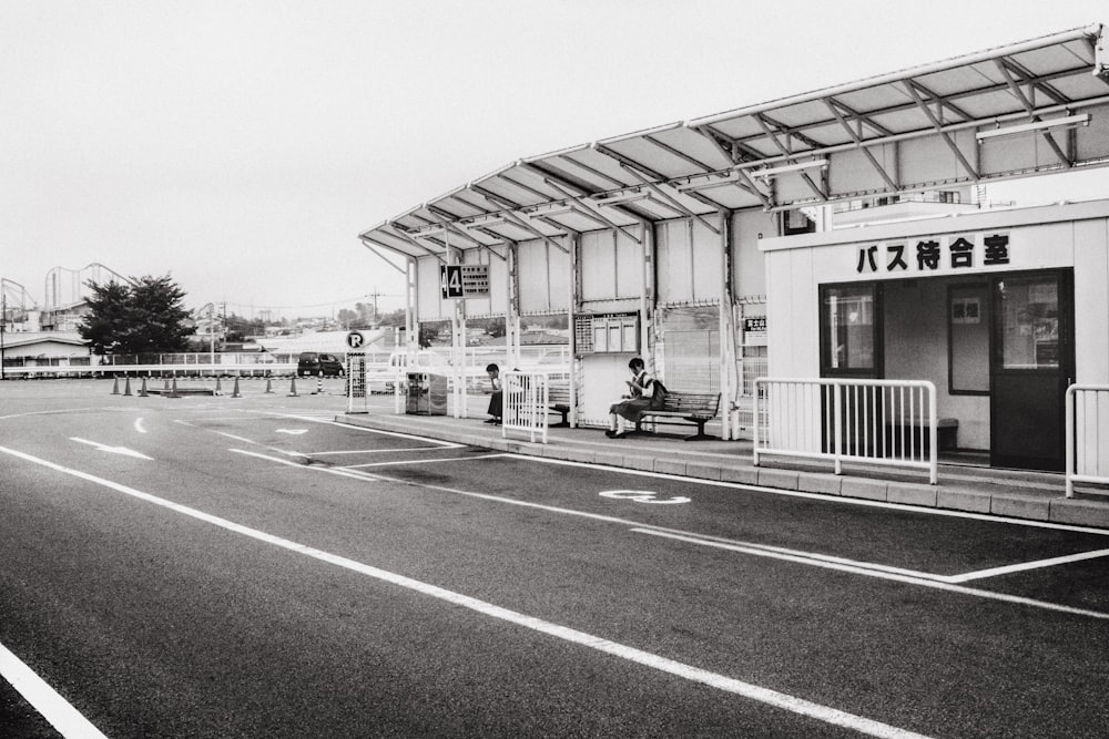 grayscale photo of two person sitting on bench near building