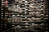 Rows of wine bottles are stored horizontally on metal shelves. The reflective glass and dim lighting create a luxurious atmosphere, with a focus on the variety and quantity of bottles.