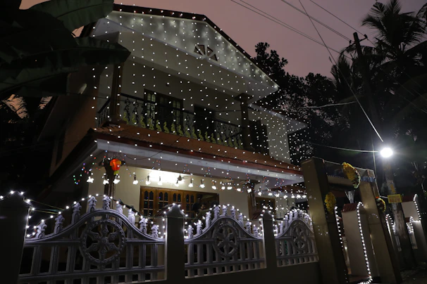 A front yard decorated with a 'Happy Anniversary' sign framed by twinkling fairy lights at dusk.