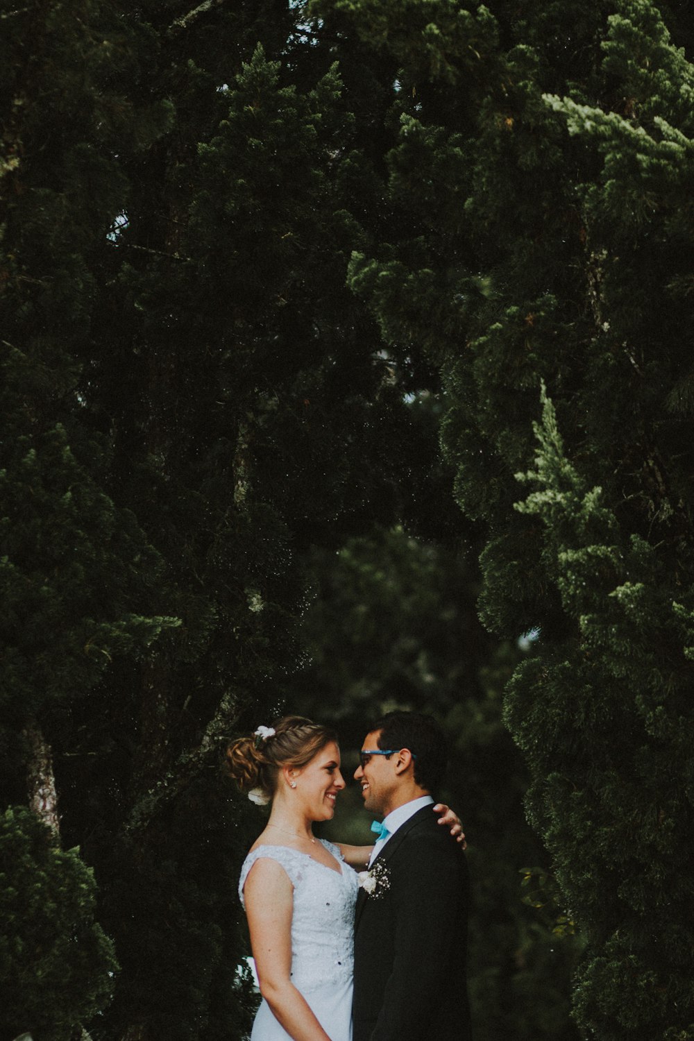 smiling woman standing near smiling man and putting her hand on back of man near green trees