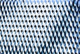 A facade of a building is covered with a repetitive pattern of geometric shapes. Each element consists of diamond shapes and triangular facets, creating an illusion of texture and depth with reflective surfaces. The elements are predominantly in shades of blue and white.