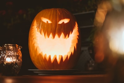 lit jack-'o-lantern beside glass candle holder with lit candle pumpkin zoom background