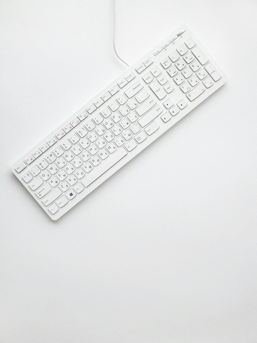 Teclado de ordenador con cable blanco sobre superficie blanca