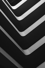 Several parallel, curved lines create a geometric pattern in a grayscale palette. The lines alternate between bright whites and dark grays, forming an abstract composition with sharp angles.