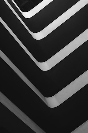 Several parallel, curved lines create a geometric pattern in a grayscale palette. The lines alternate between bright whites and dark grays, forming an abstract composition with sharp angles.