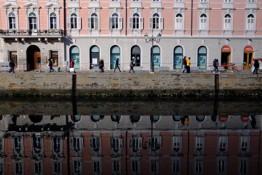 a group of people walking on a sidewalk next to a body of water