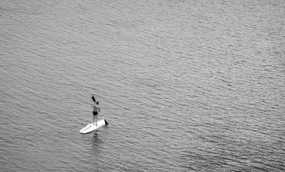 grayscale photography of person riding on board while holding oar