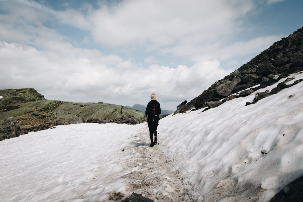 Mann im schwarzen Hemd geht auf Schnee unterhalb des Hügels