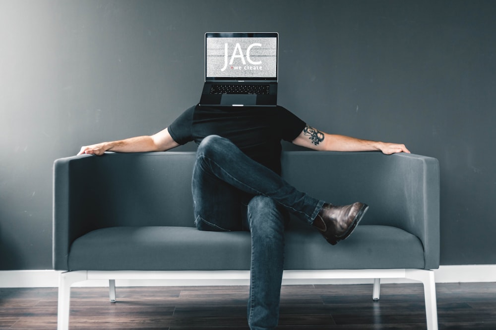 man in black shirt and blue jeans sitting on gray sofa with JAC mask