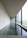 A modern and minimalist interior space featuring a long rectangular pool of water alongside a large window. The design is characterized by clean lines, polished concrete surfaces, and an overall sense of tranquility. Natural light softly illuminates the room through the window, creating reflections on the water.
