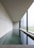 A modern and minimalist interior space featuring a long rectangular pool of water alongside a large window. The design is characterized by clean lines, polished concrete surfaces, and an overall sense of tranquility. Natural light softly illuminates the room through the window, creating reflections on the water.